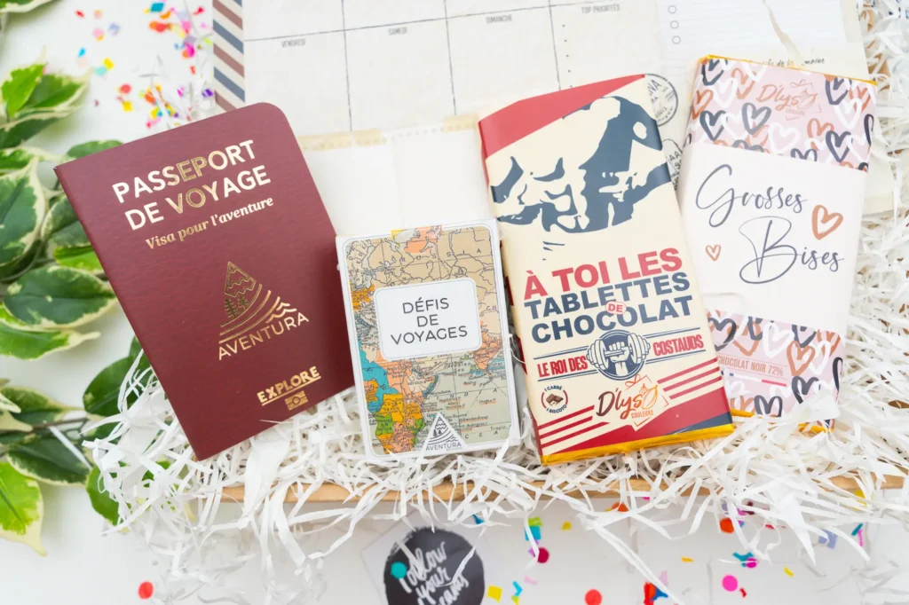 cadeau box voyage personnalisé comprenant une tirelire "travel the world", un planner de la semaine, un passeport notes, un jeu de cartes "défis de voyage" et une tablette de chocolat